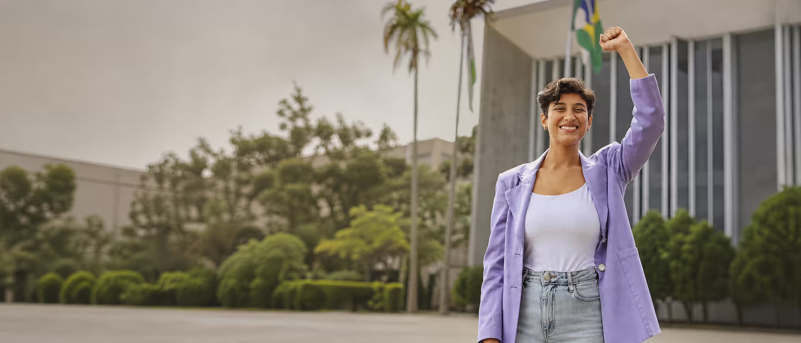 Bia Alcantara sorrindo com o punho erguido em frente à Câmara de Cascavel